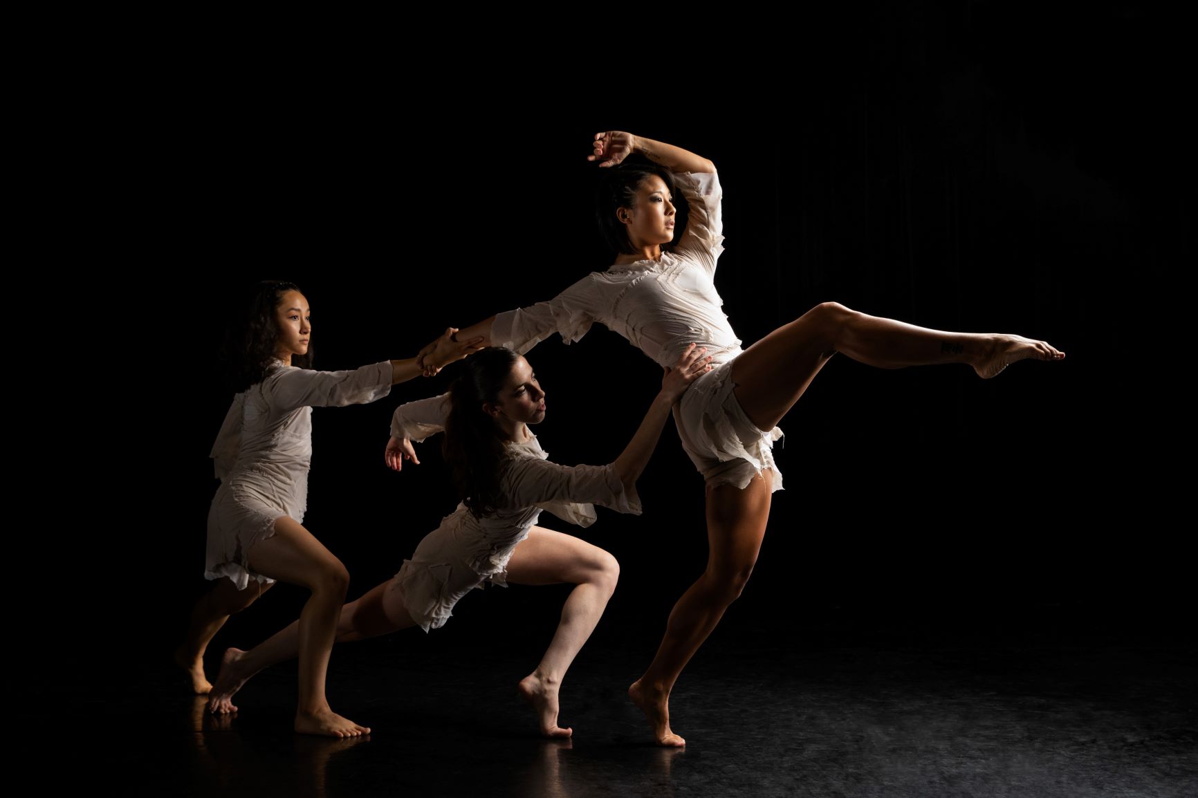 Three female dancers in white form a diagonal each with one knee bent